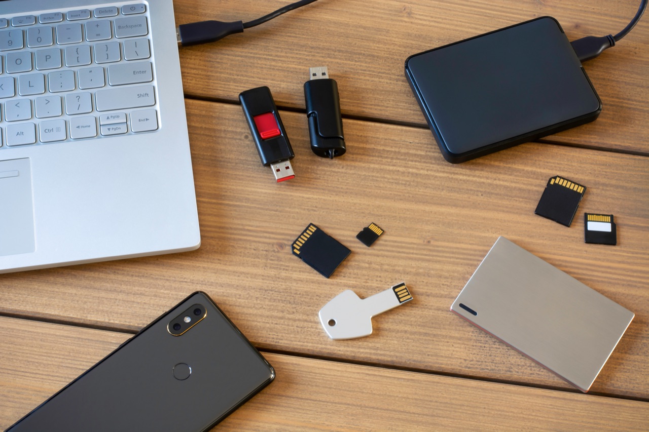 USB-Sticks, SSD, SD-Karten, Notebook und Smartphone auf einem Holztisch